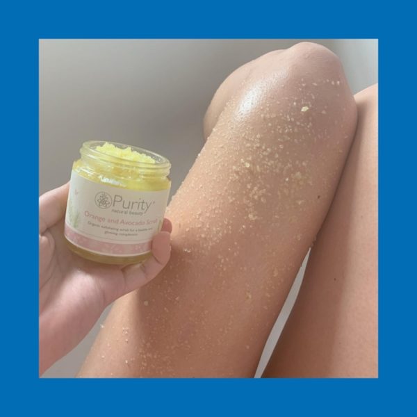 An open Jar of Orange and Avocado Scrub shown with the scrub applied to bare legs